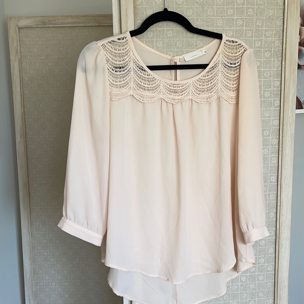 Blush pink polyester blouse. Lace trim at neckline, 3/4 sleeves, button closure.